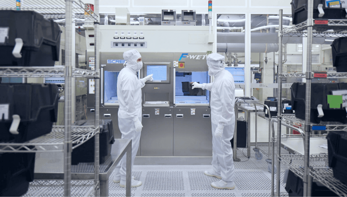 Salle blanche X-FAB — ingénieurs en combinaison stérile devant des équipements de fabrication de semi-conducteurs